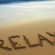 The word relax written on the beach sand.